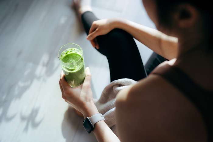 Woman sitting on the floor with a green smoothie in her hand.