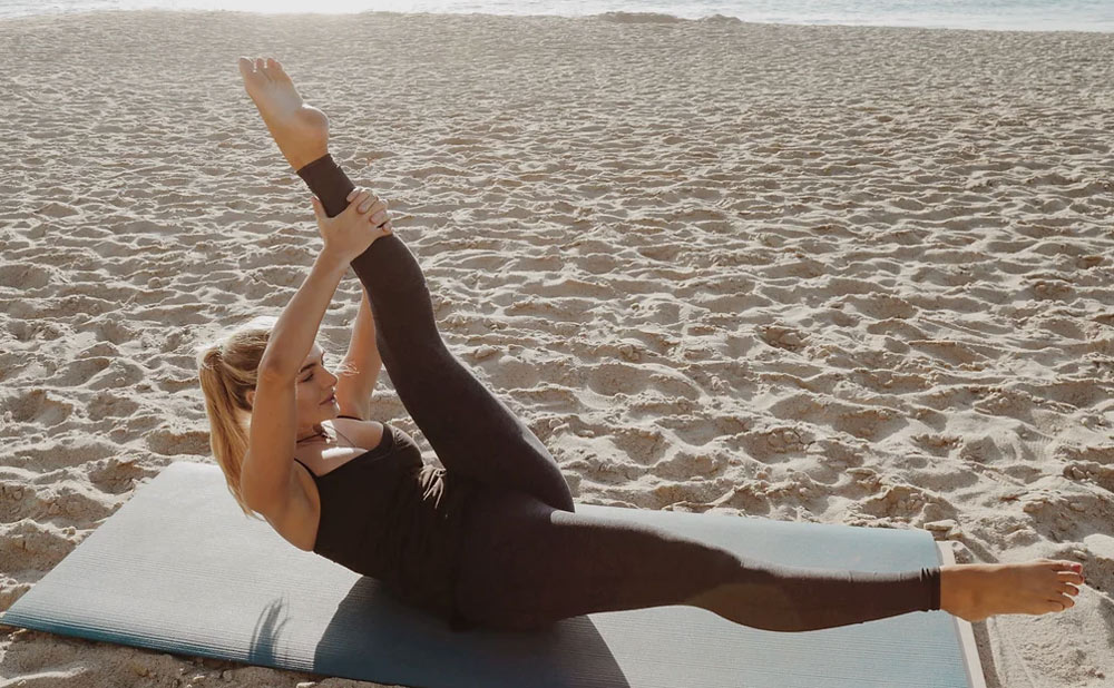 En kvinna gör yoga på stranden